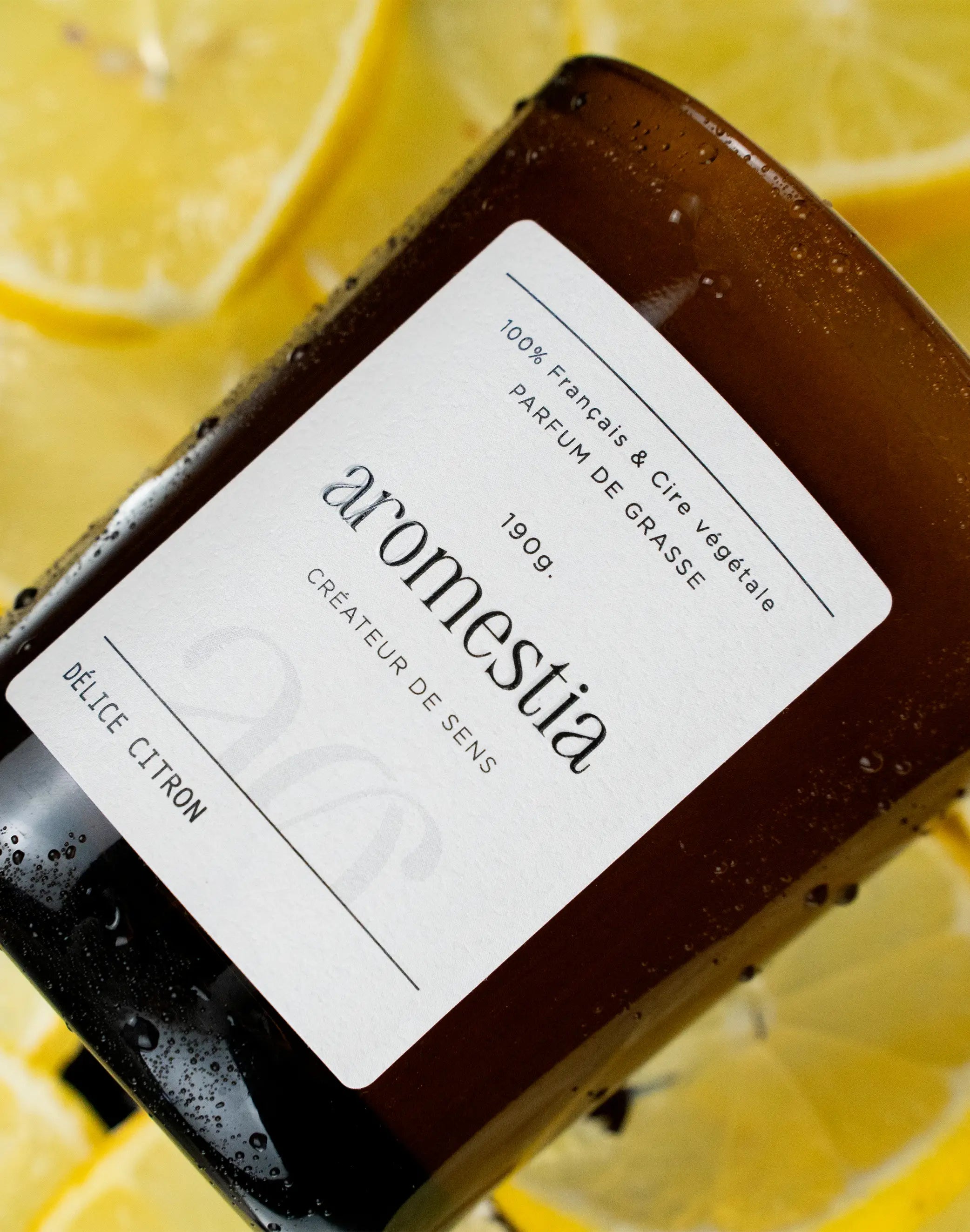 Bougie au citron Aromestia avec un contenant ambré et des citrons en arrière-plan