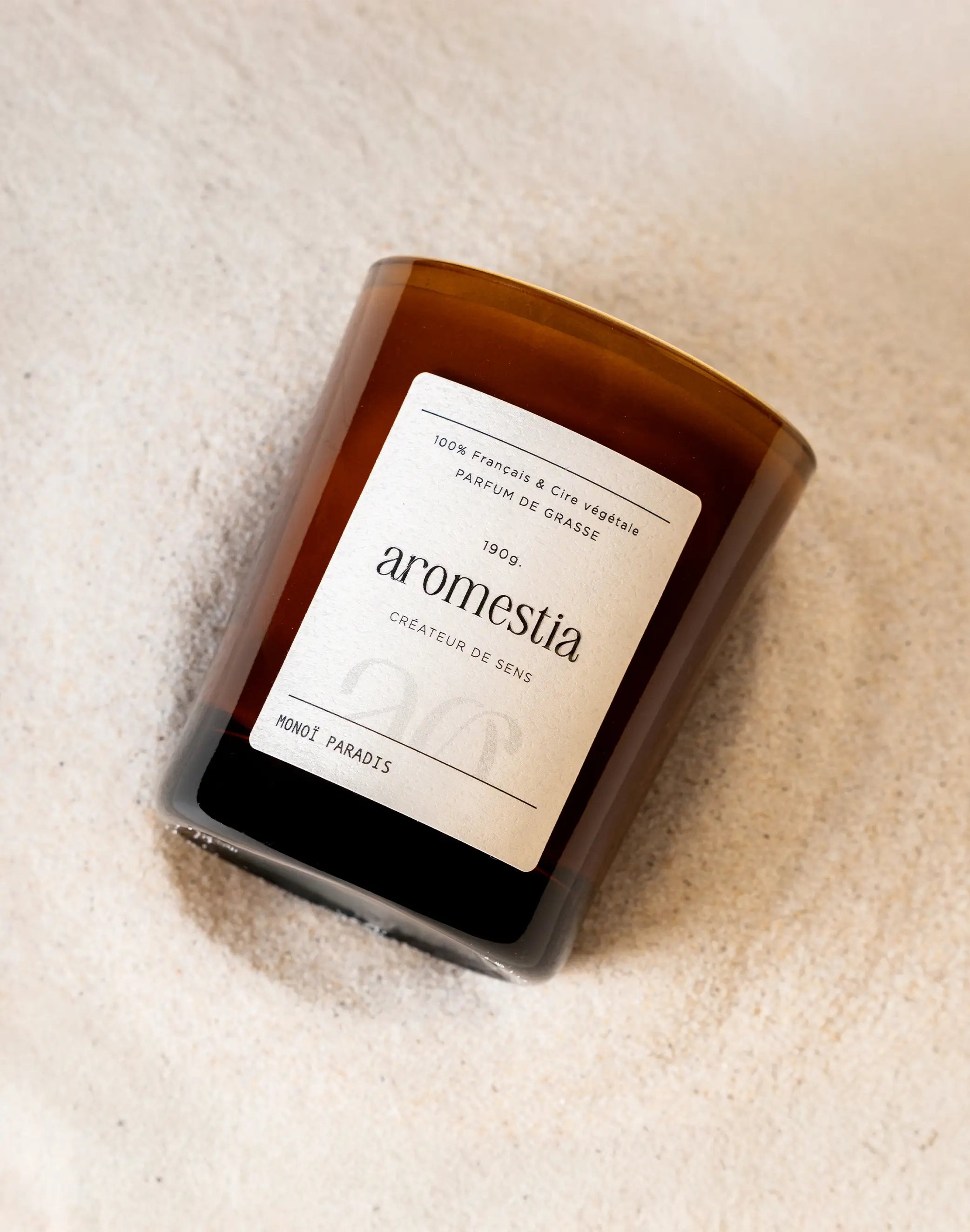 Bougie au monoï Aromestia présentée sur du sable