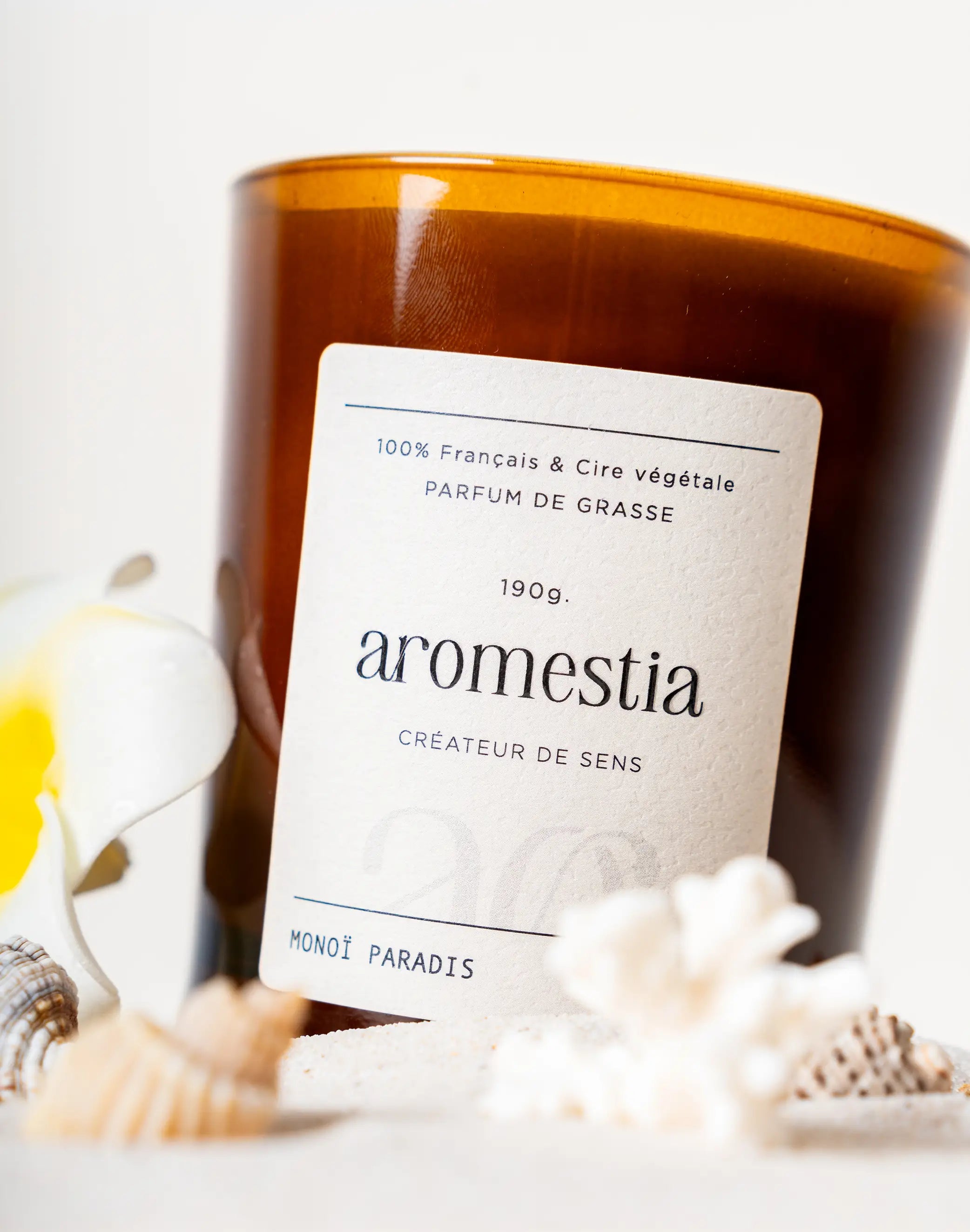 Bougie parfumée au monoï Aromestia avec des coquillages autour